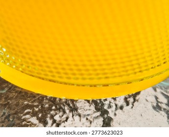 Abstract yellow geometric pattern background featuring a textured glass lens with circular indentations and natural light.