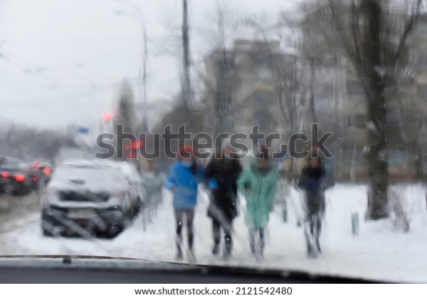 Abstraction.Blurred urban view with cars,\
traffic lights, unfocused silhouette of passersby,buildings through\
rain streams on windshield of the car. Driving in rain. Conceptual\
bad weather\
background.