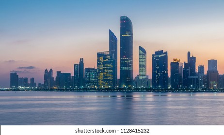 Abu Dhabi City Skyline With Skyscrapers Before Sunrise With Water Reflection Night To Day Transition Timelapse From The Breakwater Near Cultural Village. Few Clouds On Morning Sky