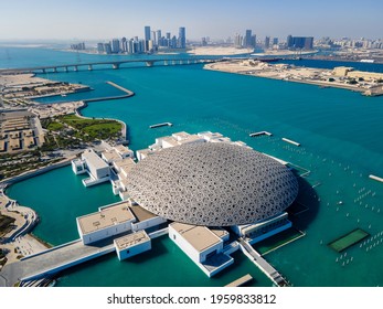 Abu Dhabi, United Arab Emirates - April 6, 2021: Louvre museum and Abu Dhabi aerial cityscape rising from the seaside water at the United Arab Emirates capital at sunrise