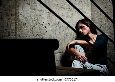 Abused woman in the corner of a stairway comforting herself