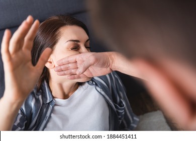 Abuser slapping wife near couch on blurred background at home