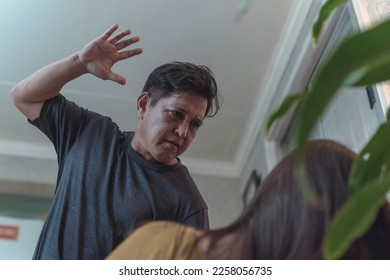 An abusive man threatens to violently slap his wife cornered on the couch. Example of intimate partner violence. - Shutterstock ID 2258056735