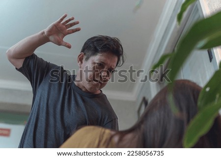 An abusive man threatens to violently slap his wife cornered on the couch. Example of intimate partner violence. Stock photo © 