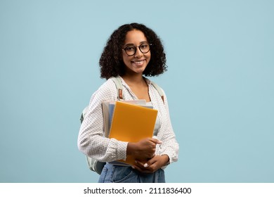 Academic education. Pretty black female student with backpack and notebooks smiling at camera over blue studio background. Young African American woman ready to start university