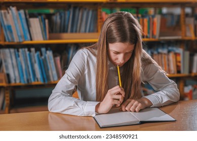 Academic teen girl studying in the library, solving assignments, writing and erasing answers in a notebook. Concept of knowledge and school.