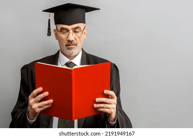 Academician, Professor, Prof Is Wearing A Cap With Tassel And Black Gown. Senior Educator Holding Red Folder. Doctor Of Philosophy, Learned Man From A University Or College.