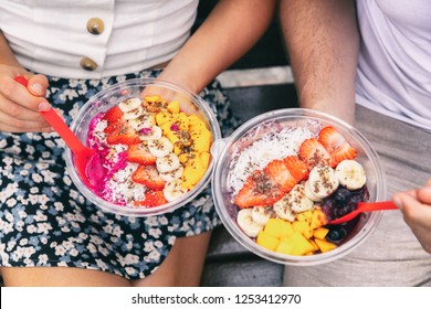 Acai Bowl And Pitaya Dragonfruit Smoothie Healthy Breakfast Bowls Young Friends Eating Together. Couple Man And Woman Eating Sitting Outside In Park For Lunch Break. Closeup On Food.