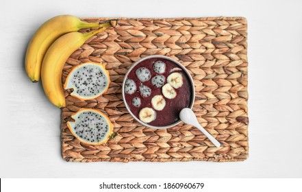 Acai smoothie bowl with fresh pitaya balls and sliced bananas topping on frozen treat. Healthy organic breakfast top view at home.
