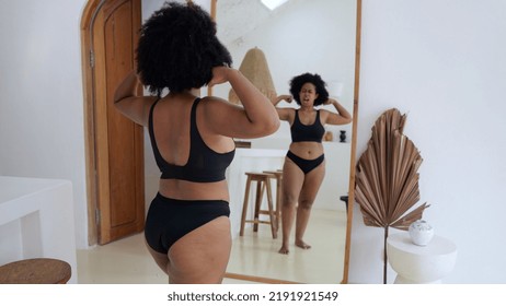 Acceptanceof A Woman Of Obesity. A Black Woman In Front Of A Mirror In Black Lingerie Looks At Her Magnificent Forms And Her Body Likes Her. The Concept Of Body Positivity.