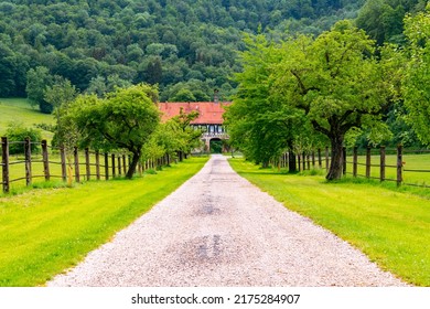 Access to historic monastery farmhouse with picturesque alley way and half timbered facade. Tourist attraction near “Uracher Wasserfall“ cascade in rural landscape in Germany with pasture and meadows.