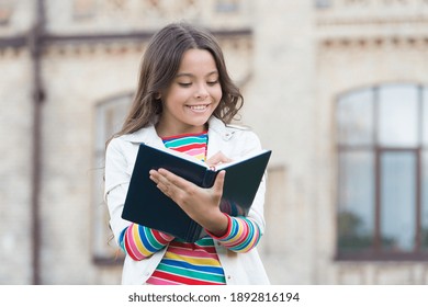 Access to much more than just book. Knowledge concept. Little girl hold book. Girl with book school building background. Book from library. Making notes. Inspired poet. Talented cute schoolgirl.