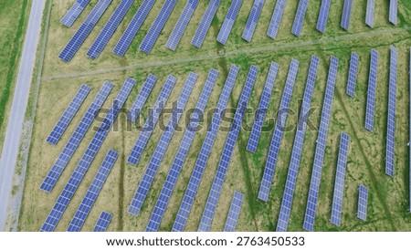 Access road solar rows run beside paved lane near Creamery Road within the Emmitsburg industrial corridor. Dark panels, grassy corridors and uniform spacing form strong linear textures, Maryland. USA