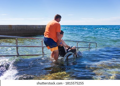 Accessible Beach With Ramp For Disabled People. Man On Wheelchair Going Swimming.