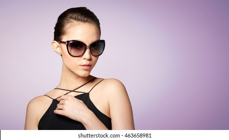 accessories, eyewear, fashion, people and luxury concept - beautiful young woman in elegant black sunglasses over violet background