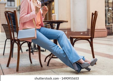 accessories of stylish woman sitting in cafe, legs in blue jeans, high heeled shoes, handbag, spring summer fashion trend elegant style