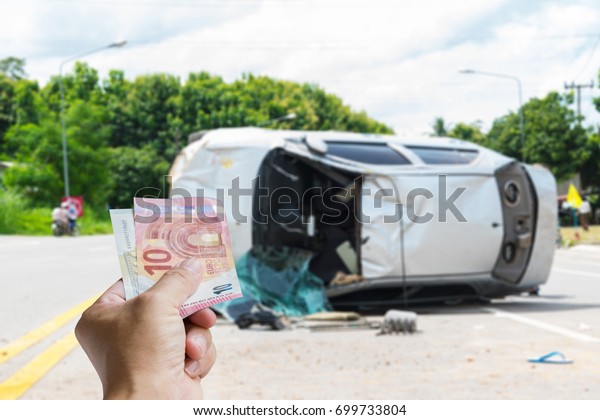 Accident insurance can help you when needed.\
Men hold cash, blur image of the old car accident scene upside down\
on the road as\
background.