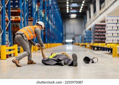 Accident on a workplace. A warehouse worker is lying on the ground and manager trying to help him. - Shutterstock ID 2255975087