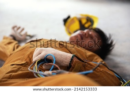 Accident from work of electrician or maintenance worker lying unconscious on floor while holding electric wire and tensed hands in the factory control room after the shock. Electronic Injury concept