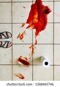 Accidentally Broken Glass Bottle Of Spilled Bright Red Tomato Sauce On White Tile Floor With Roll Of White Paper Towel, Visible Feet Of Woman Looking Down At The Mess, Scene Viewed From Above Down