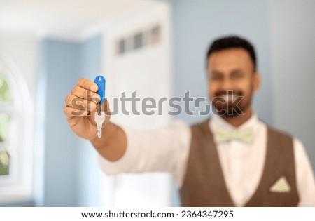 Accommodation Offer. Unrecognizable Middle Eastern Receptionist Man Holding And Showing Room Key To Camera, Posing In Formal Uniform Standing At Hotel Reception Indoors. Shallow Depth