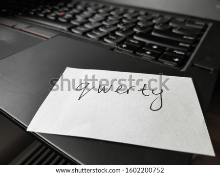 Account security concept. Password written on a paper sticker with a marking pen. Weak password. Qwerty - most commonly used password. Password on piece of paper with laptop keyboard as background.