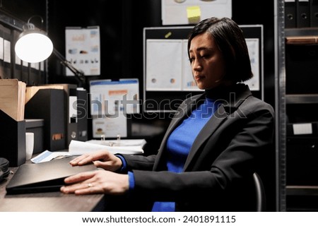 Accountancy asian employee clocking out from work, shutting down laptop in business office. Bookkeeper executive in archival depository filled with cabinet, folders and flowcharts