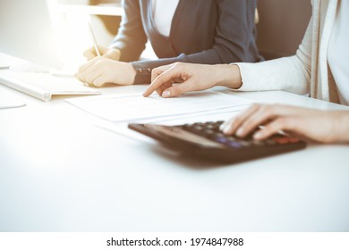 Accountant checking financial statement or counting by calculator income for tax form, hands closeup. Business woman sitting and working with colleague at the desk in office. Tax and Audit concept
