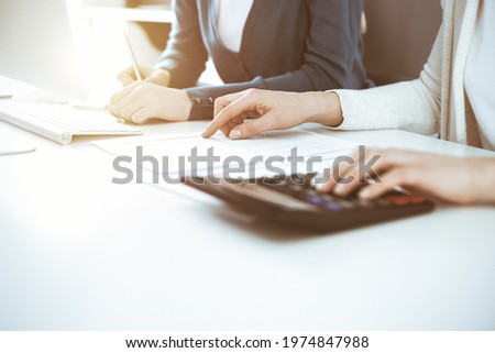 Accountant checking financial statement or counting by calculator income for tax form, hands closeup. Business woman sitting and working with colleague at the desk in office. Tax and Audit concept