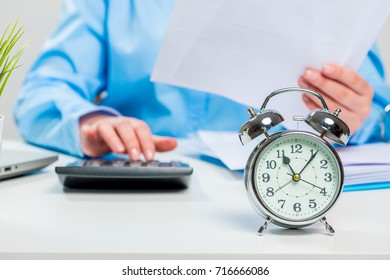 Accountant with papers and calculator working in the office, alarm clock close-up of focus in focus - Shutterstock ID 716666086