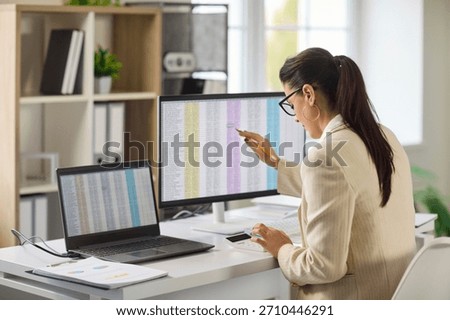 Accountant performs audit analysis on office computer. Woman reviews spreadsheet data, uses calculator, validates accuracy and compliance in office. Clear concept finance control and reporting.