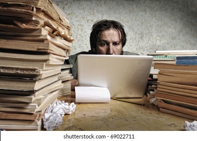 Accountant In Problems. Alone Working On Laptop With A Lot Of Books Around On Messy Table.