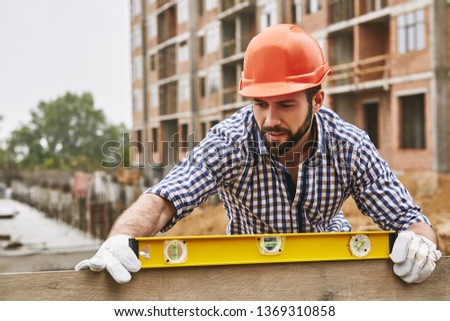 Accuracy and quality. Construction worker in protective yellow helmet checking the level of a plank of wood. Measurement concept