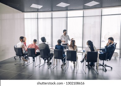 Achieving best results after annual refresher course. Indian young business mentor conducting a business training while standing in front of people sitting in row at meeting room. - Shutterstock ID 1302108616