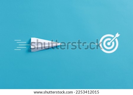 Achieving goals. Following the right route to intended business objectives. Paper airplane moves towards the target goal symbol on blue background.