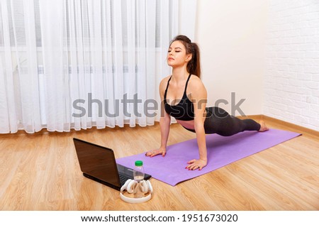 Achieving sound of mind through yoga. Young sporty woman practicing yoga. Woman exercising at home in front of her laptop. Attractive sporty woman practices yoga asana at home. Girl meditating