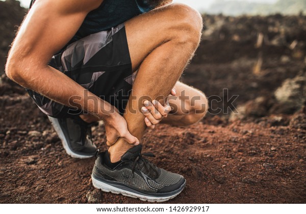 Achilles injury on running outdoors. Man\
holding Achilles tendon by hands close-up and suffering with pain.\
Sprain ligament or Achilles\
tendonitis.