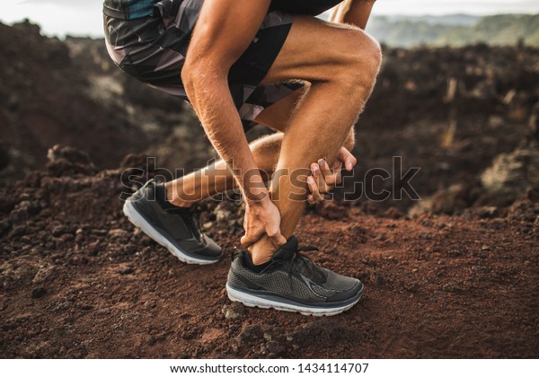 Achilles injury on running outdoors. Man\
holding Achilles tendon by hands close-up and suffering with pain.\
Sprain ligament or Achilles\
tendonitis.