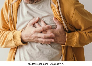 Aching heart and heart attack, adult male with painful grimace pressing the upper abdomen with his hands to ease pain