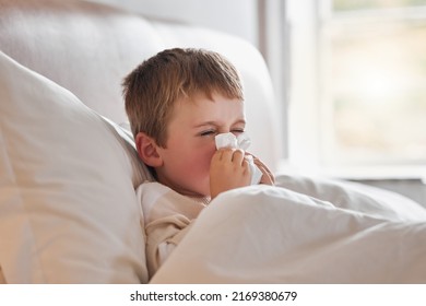 Achooo. Shot of a little boy feeling ill in bed at home and blowing his nose. - Powered by Shutterstock