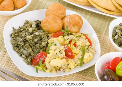 Ackee & Saltfish - Traditional Jamaican dish made of salt cod and ackee fruit. Served with callaloo and johnny cakes. Patties on background.