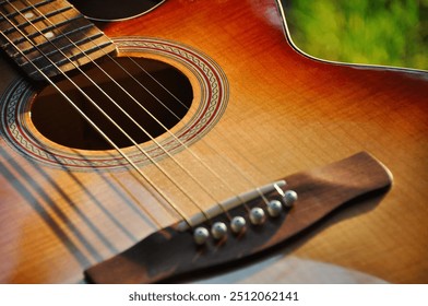 Acoustic guitar. Close-up image of old acoustic guitar in a garden: shiny brown deck instrument with metal and nylon strings over fretboard. - Powered by Shutterstock