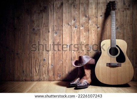 Acoustic guitar, cowboy hat and boots resting against a blank wooden plank grunge background with copy space