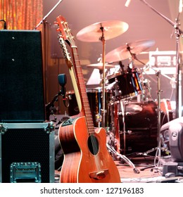 Acoustic Guitar, Drum Kit, Loudspeaker And Other Musical Equipment On Stage Before Concert. Red Light. Concept Image. Night Club, Performance, Music Band, Singing, Profession, Art, Instrument