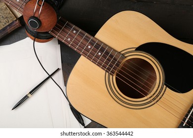 Acoustic guitar, headphones, musical notes and white papers on wooden background, close up - Powered by Shutterstock