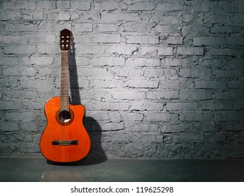 Acoustic guitar leaning on grungy gray brick wall - Powered by Shutterstock