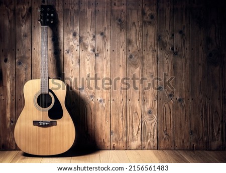 Acoustic guitar resting against a blank wooden plank grunge background with copy space
