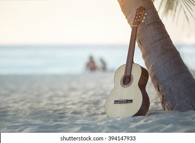 Акустическая гитара, стоящая на песчаном пляже под пальмой