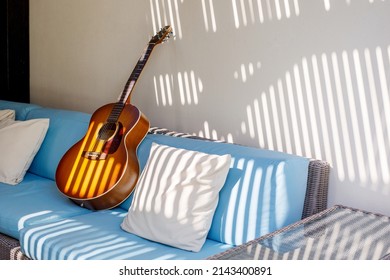 An acoustic guitar stands on a blue sofa next to a pillow on the terrace - Powered by Shutterstock