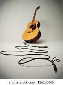 Acoustic guitar with trailing lead on white backdrop